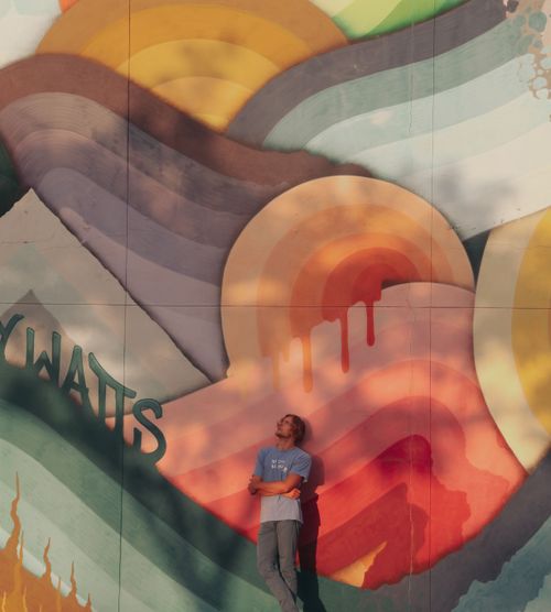 A colorful, eclectic mural behind graphic designer jake Davis, who is looking upwards.