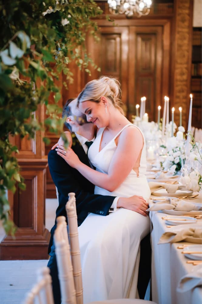 A bride and groom hugging each other in front of a long table.