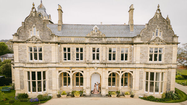 a wedding couple of people standing in front of a luxurious wedding venue, Clevedon Hall.