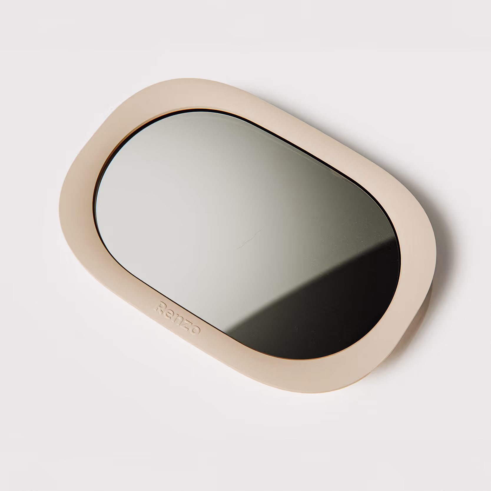 Modern and soft minimalistic design of a baby car mirror with curved almond cream colour frame and lense-like acrylic mirror. The mirror is on the white floor.