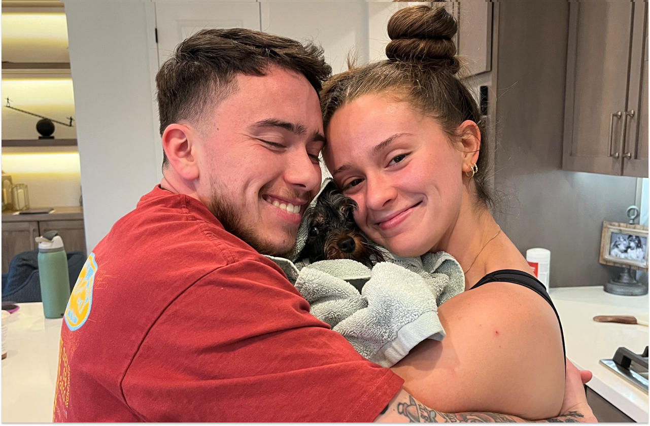 Hunter hugging his partner and dog in the kitchen