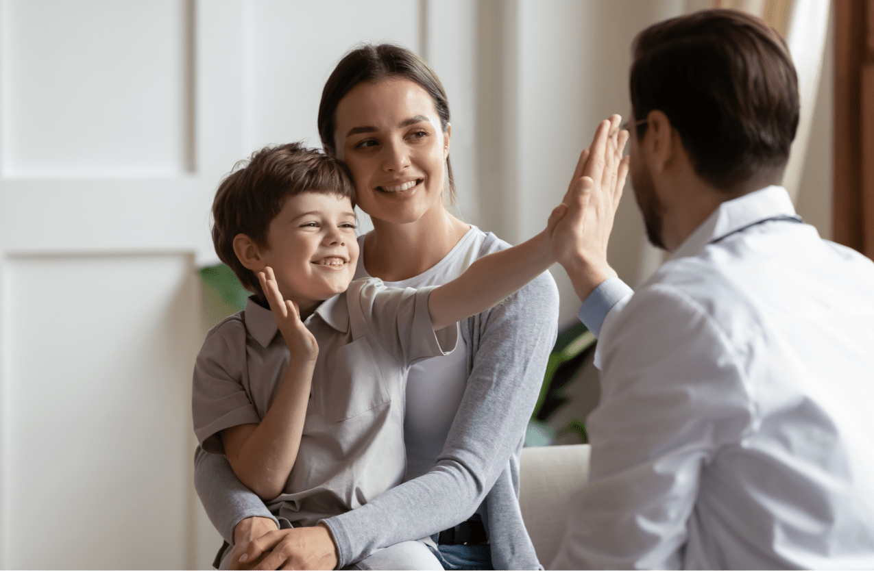 Child high-fiving doctor while in his mother's arms