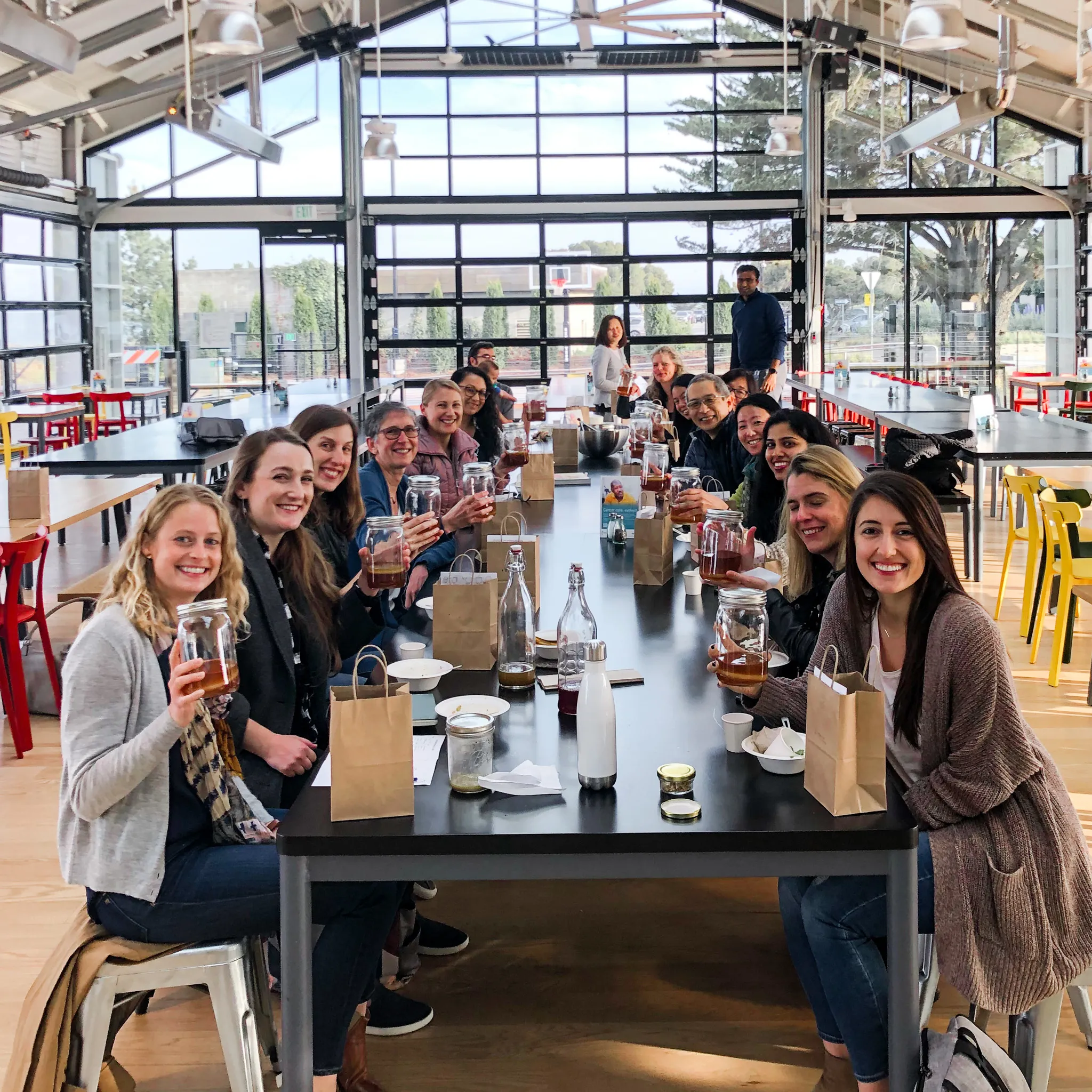 Group of people sitting at table smiling with jars during corporate kombucha workshop in San Fransisco