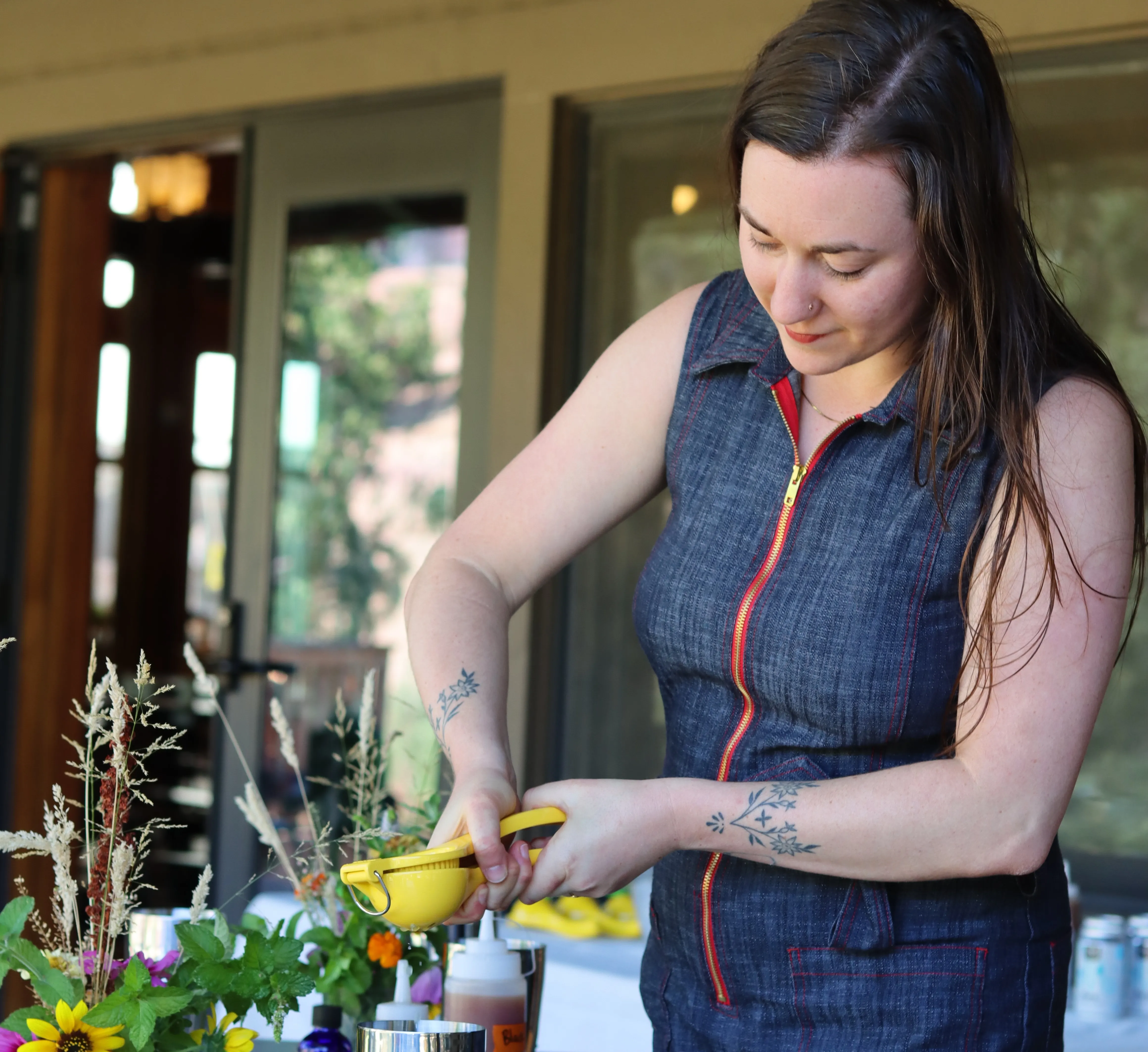 Person squeezing lime from a citrus press into a shaker during a mocktail mixology class, with shakers and ingredients on the table