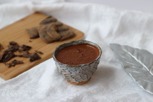 A rich chocolate elixir drink served in a ceramic cup, with cacao pieces on a wooden board, crafted during a corporate wellness mocktail mixology workshop, perfect for team building and health-focused corporate events.