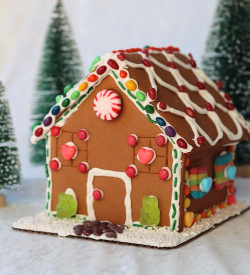 A hand holding candies, part of a virtual class with kits sent for a corporate holiday event, with pieces of a gingerbread house in the background