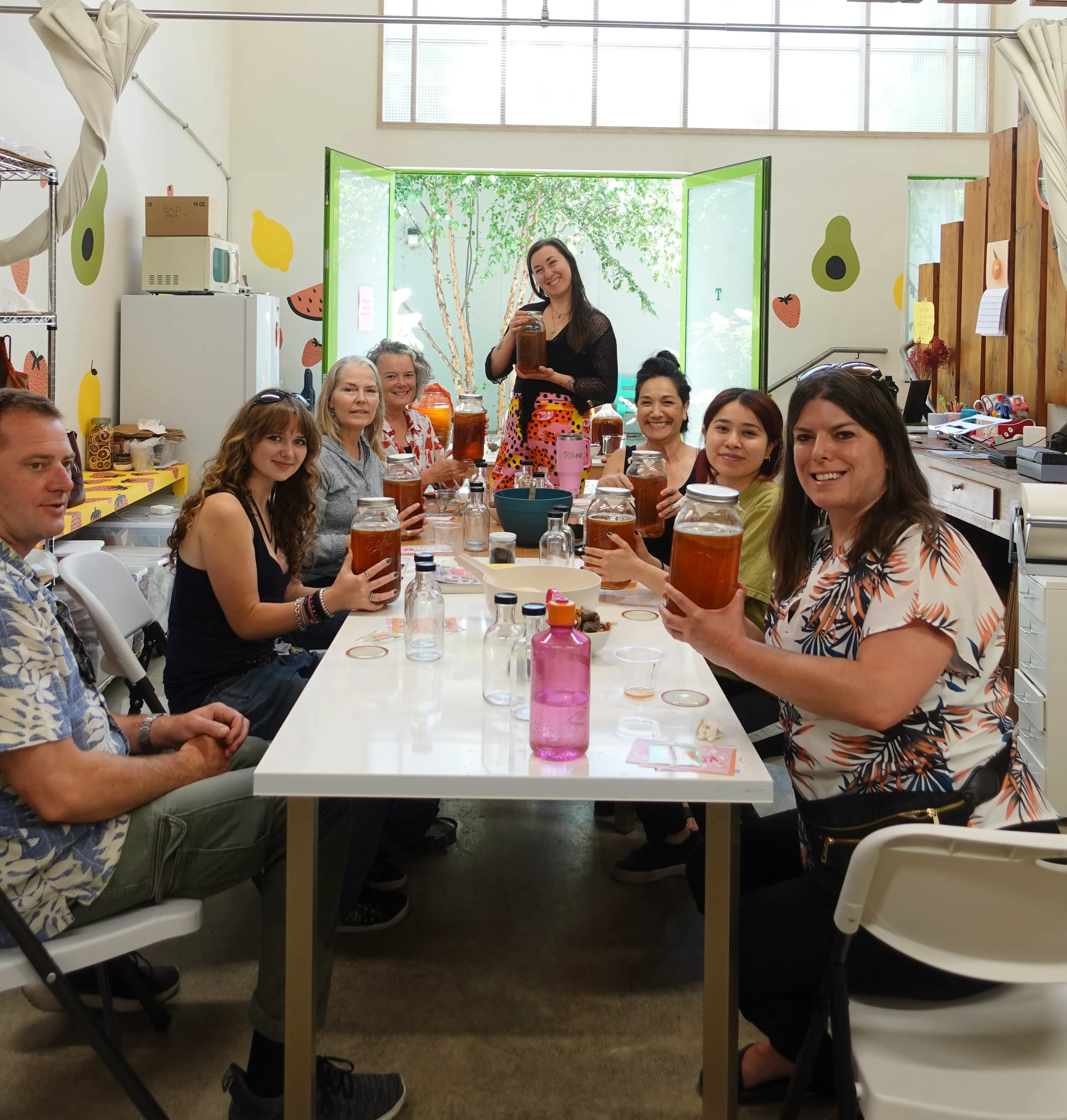 Group of smiling people holding up kombucha jars with SCOBYs during a kombucha workshop in Oakland
