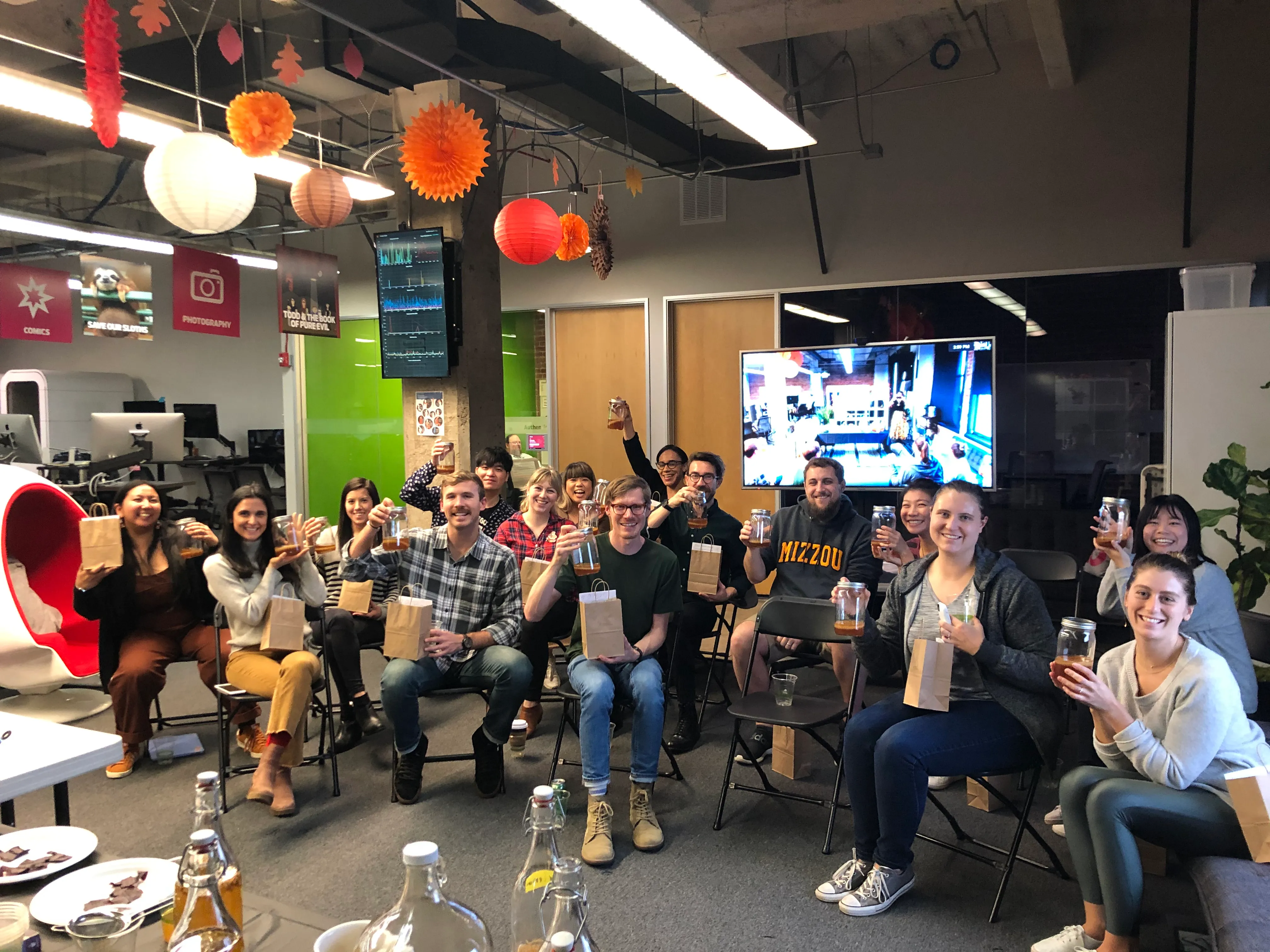 Group of coworkers raising kombucha bottles in celebration after a team building kombucha brewing class, set in an office