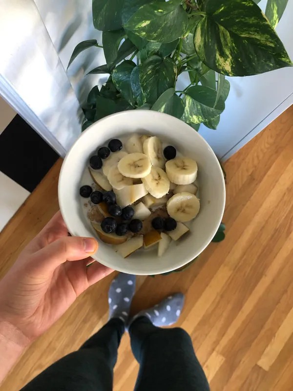A healthy breakfast bowl with blueberries and bananas being held over a wooden floor background