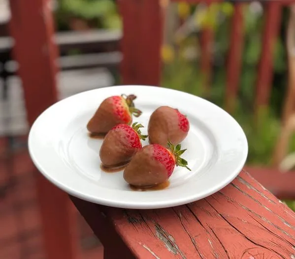 Chocolate-dipped strawberries elegantly arranged on a white plate, set against a rich red wooden background.