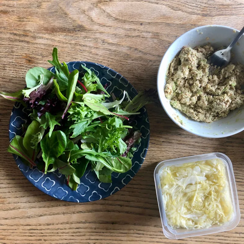 Plate of mixed greens and salmon mixed with ingredients on a wooden table