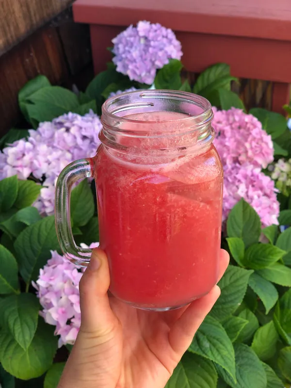 Pink mocktail in a mason jar with flowers in the background