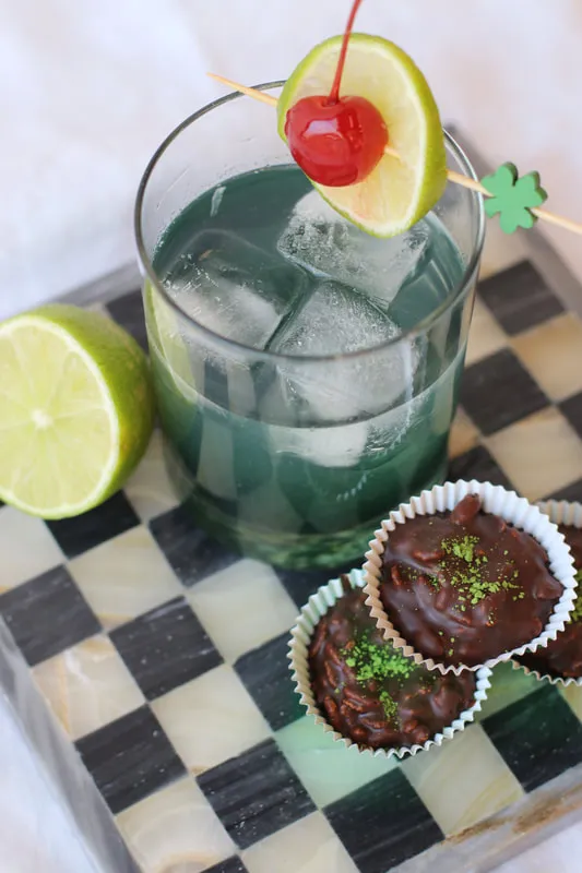 A green St. Patrick's Day mocktail, dyed with spirulina, garnished with lime and cherry, set on a checkered backdrop.