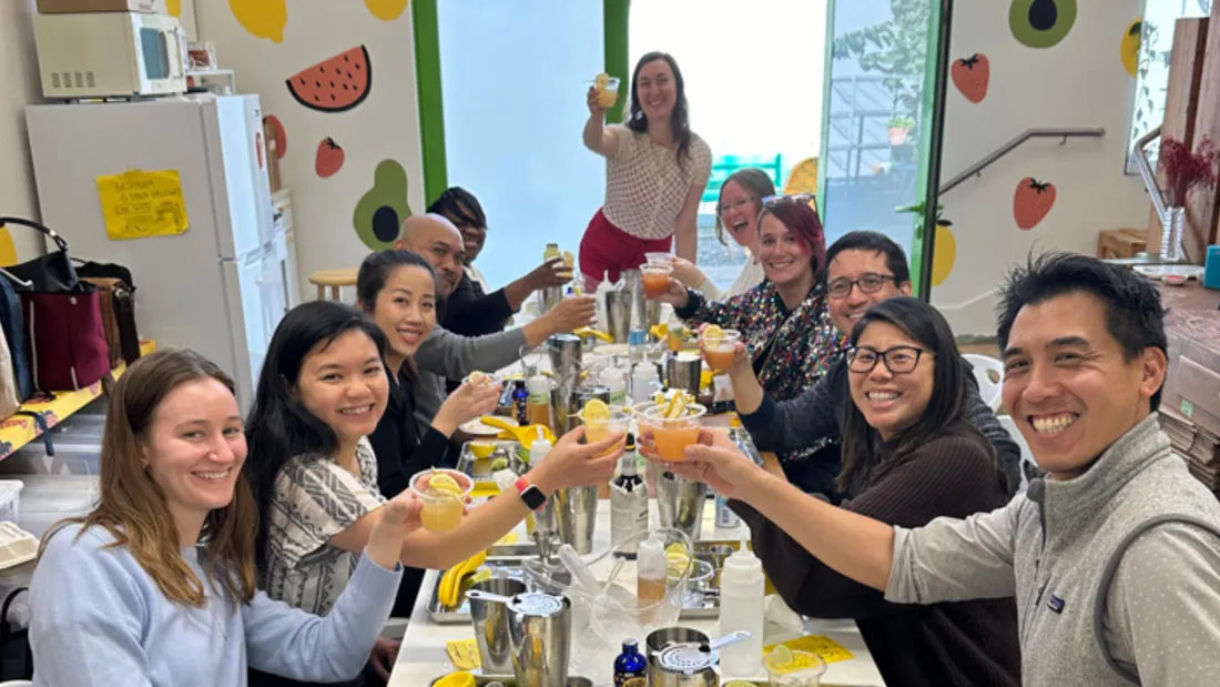 A corporate mocktail class with 11 participants raising non-alcoholic drinks and smiling, perfect for team building during a mocktail class.