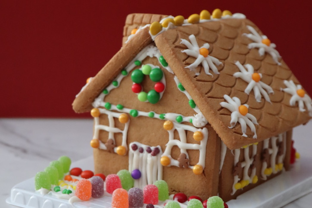 Festive gingerbread house decorated with candies with plastic trees in the background made during a corporate holiday event