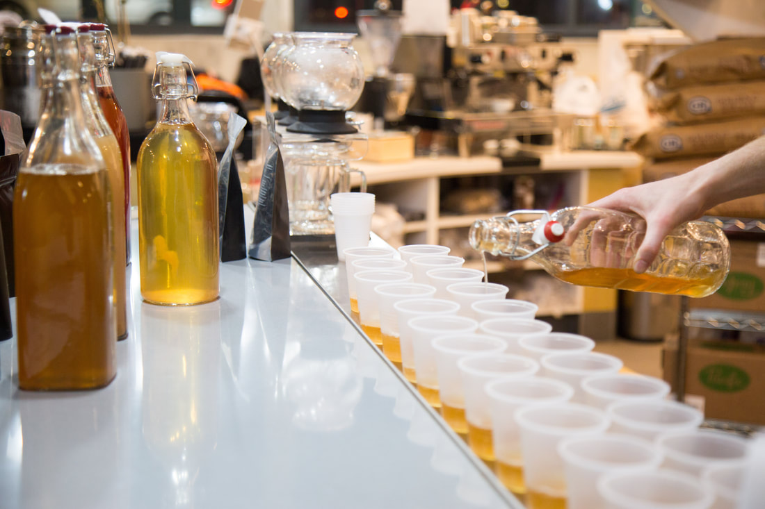 hand pouring rows of cups of kombucha at boba guys