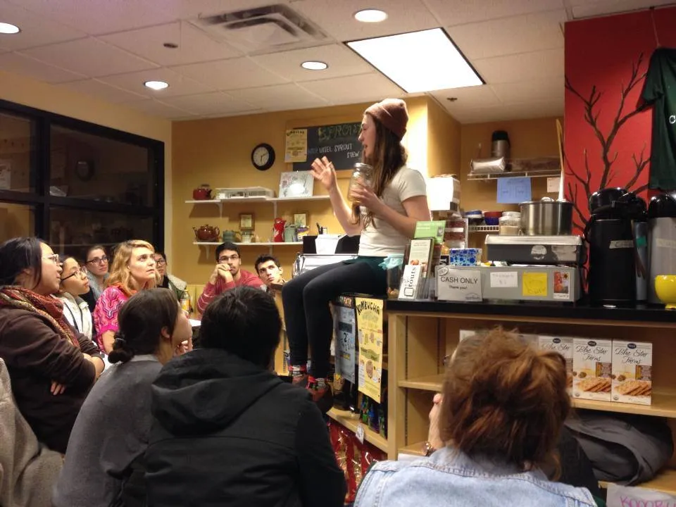 woman sitting on counter in front of group of people teaching kombucha brewing class