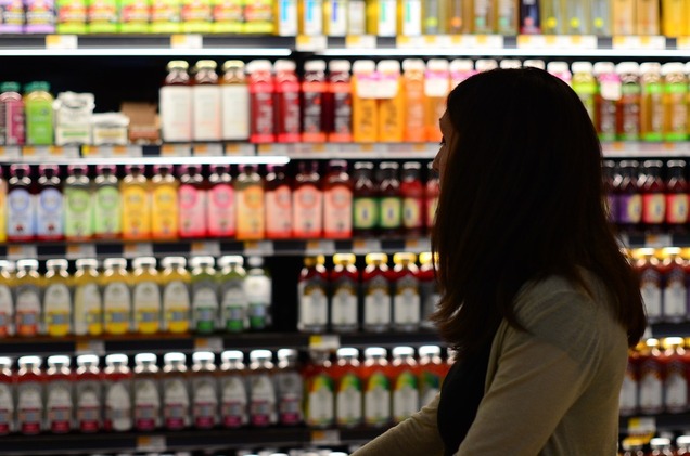 woman shopping for kombucha in grocery store in front of wall of kombucha bottles