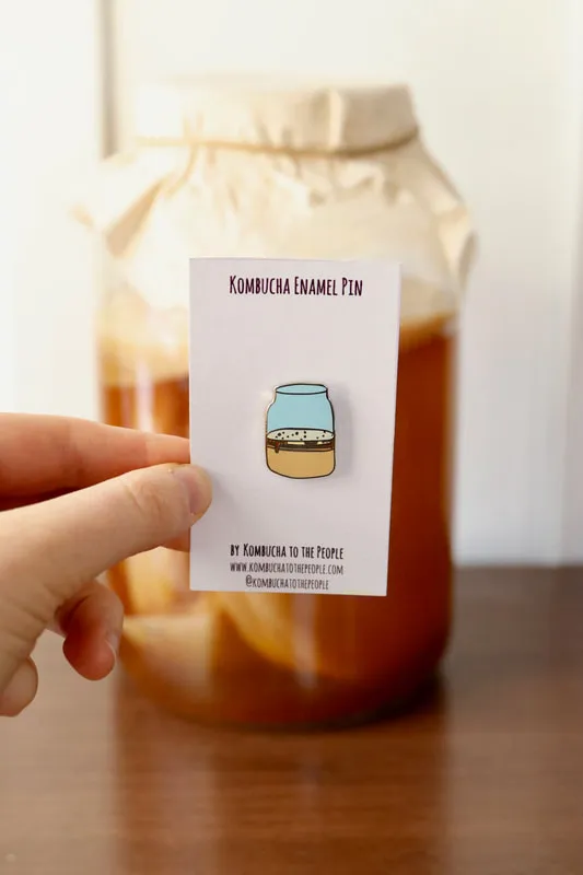 kombucha enamel pin of kombucha scoby in a jar in front of real jar of kombucha with SCOBY