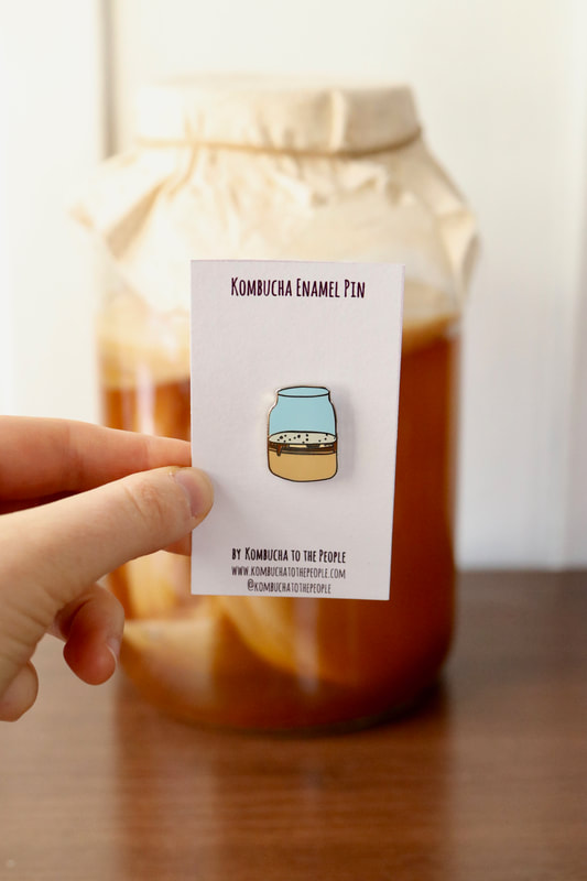 kombucha enamel pin of kombucha scoby in a jar in front of real jar of kombucha with SCOBY
