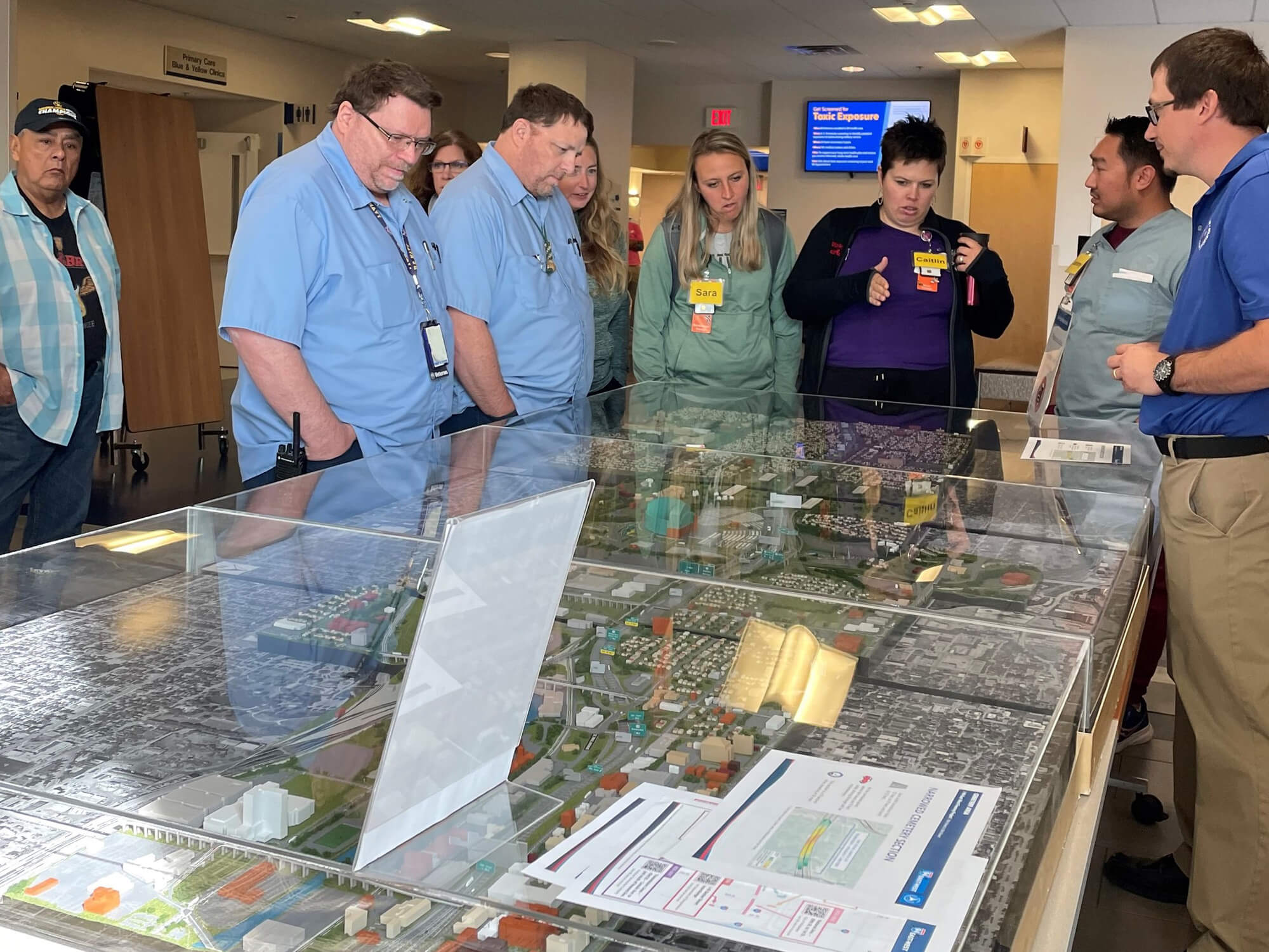 Veterans Administration staff and patients gathered around the 94 East-West project model and discussing the project with staff.