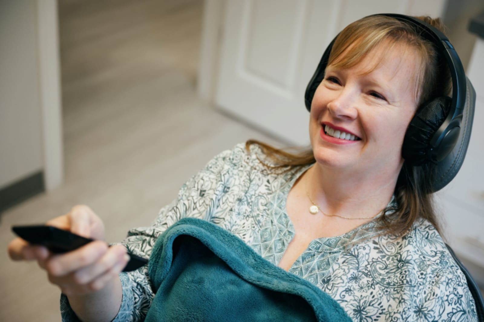 Woman wearing headphones smiling while holding a tablet device indoors.