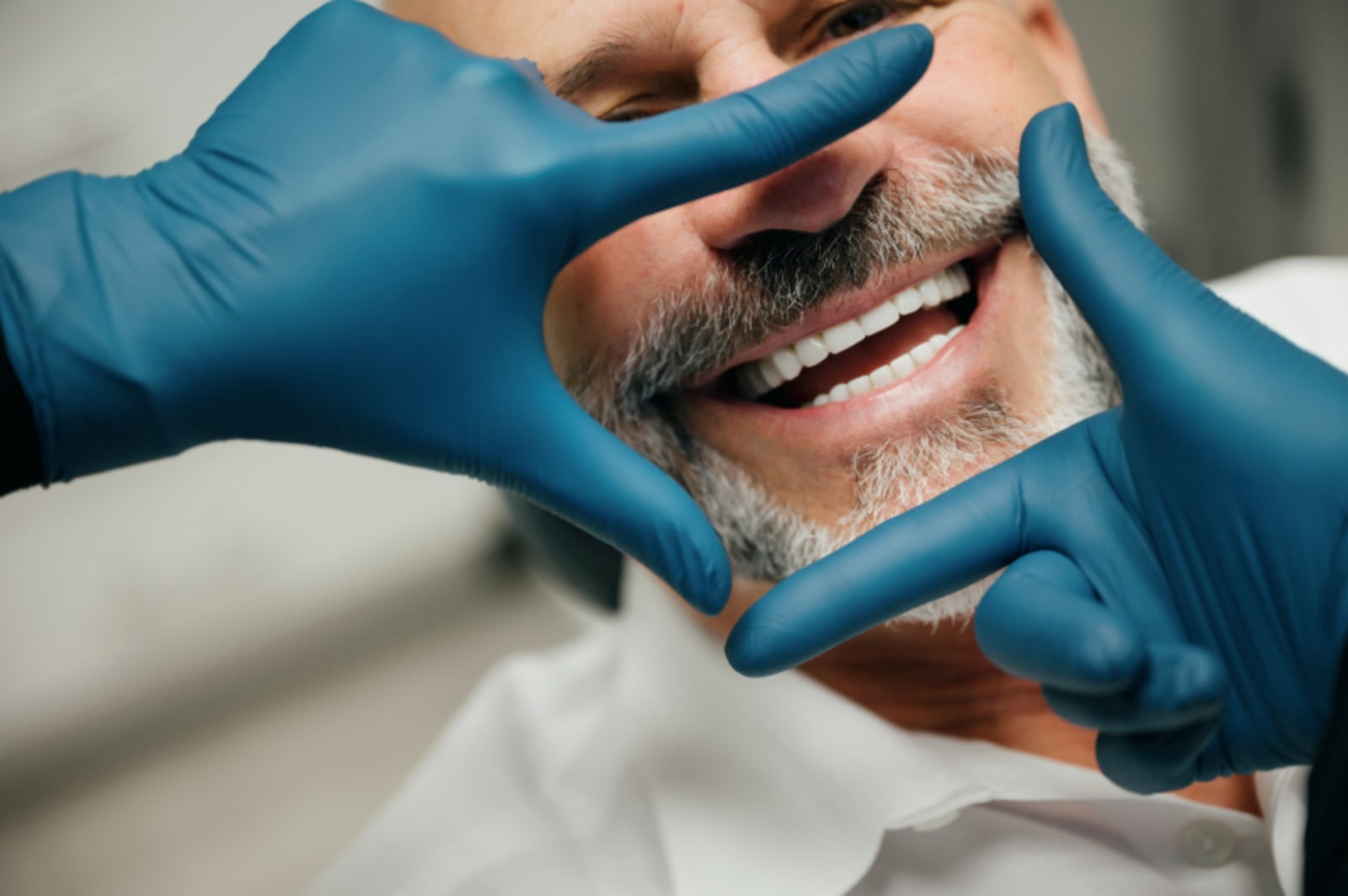 Dentist in blue gloves examining a male patient's smile during consultation.