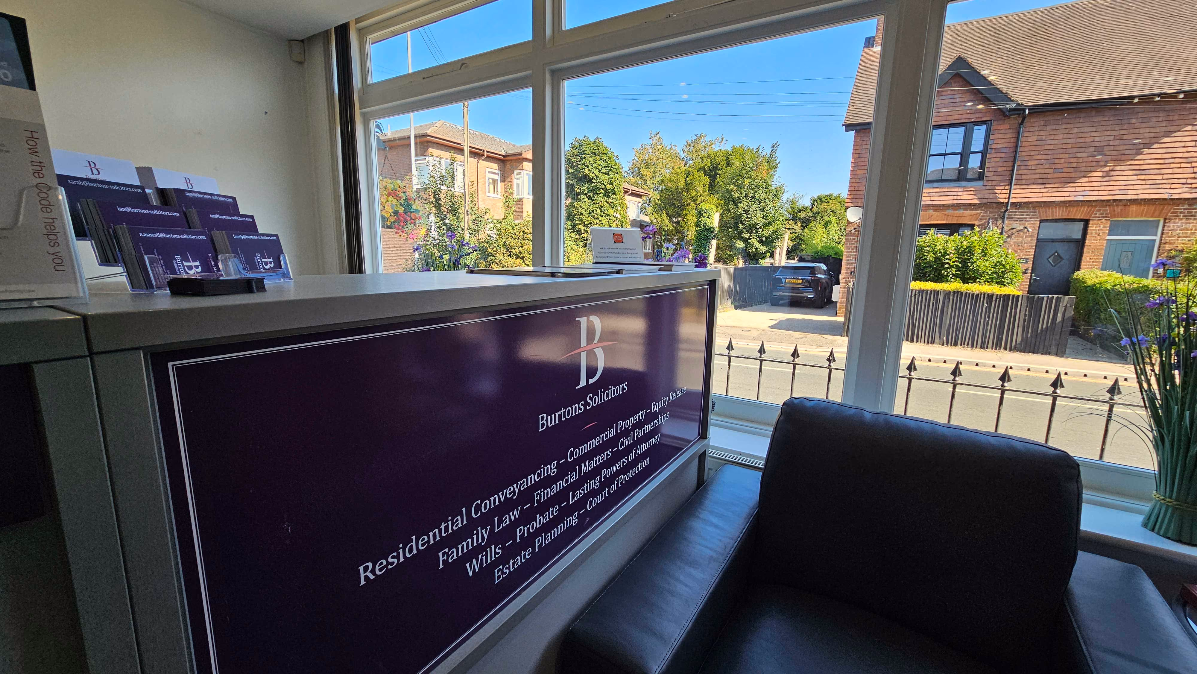 Office reception area with a counter displaying brochures, next to a large window overlooking a street.