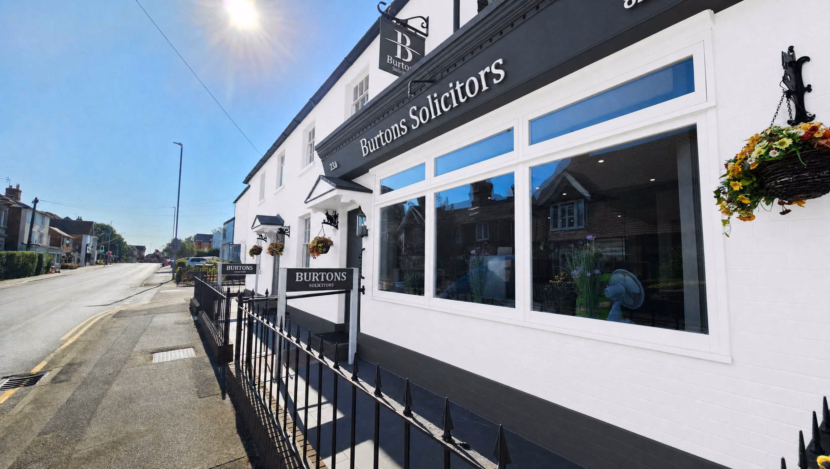 Street view of Burtons Solicitors building with large front window and hanging flower baskets.