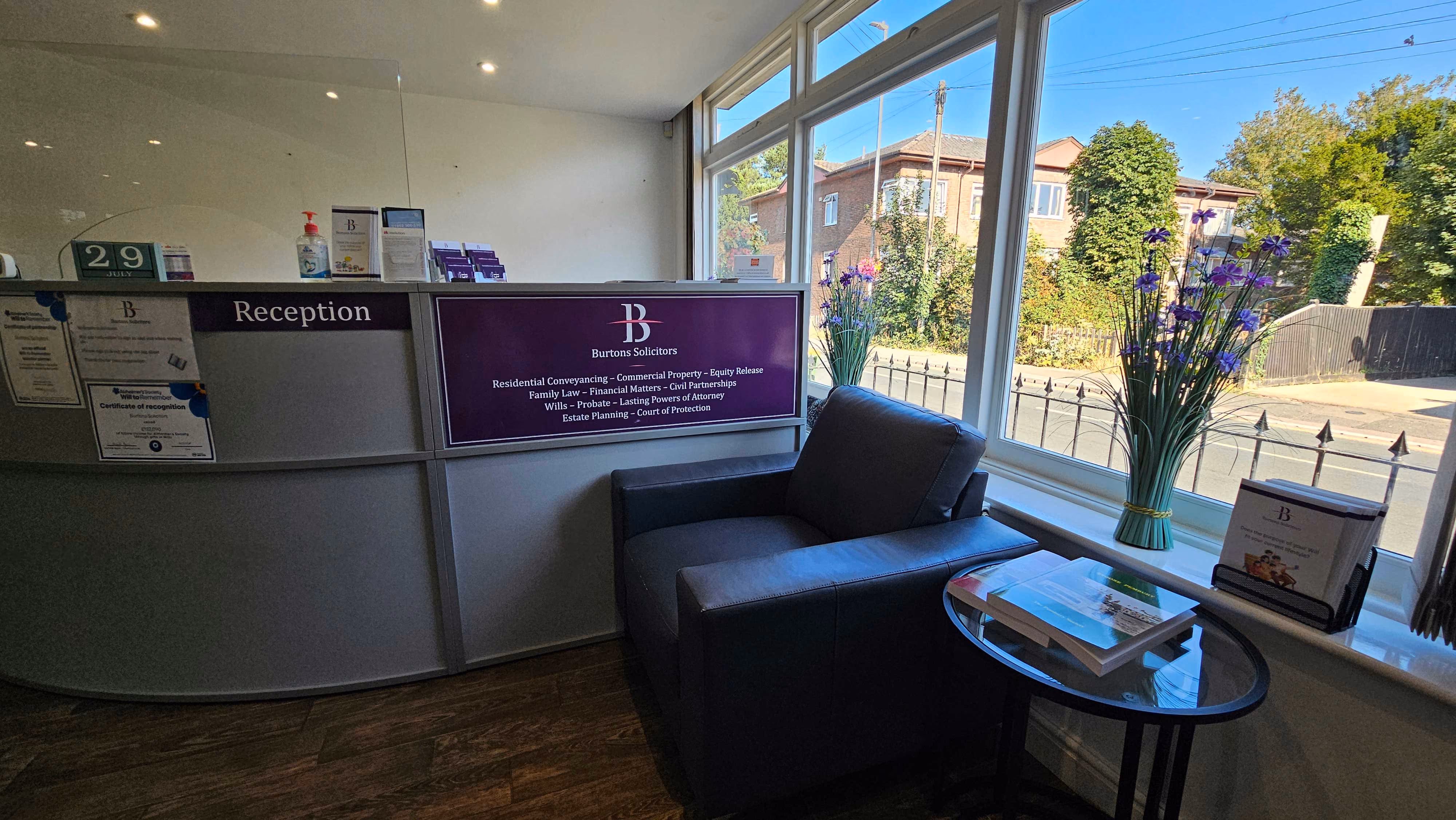 Office reception area with a counter, brochure stand, and a waiting chair beside a window.
