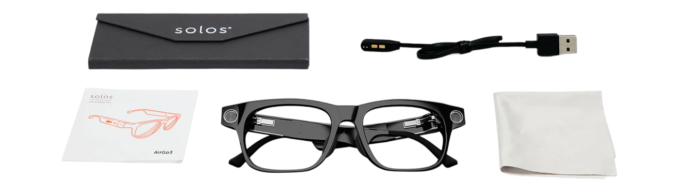 Contents of the Ally Solo glasses kit laid out on a flat surface. Includes: a black carrying case with the "Solos" logo, a magnetic USB charging cable, a user manual labeled "AirGo3", a pair of black smartglasses, a white cleaning cloth, and a soft pouch or cloth bag.
