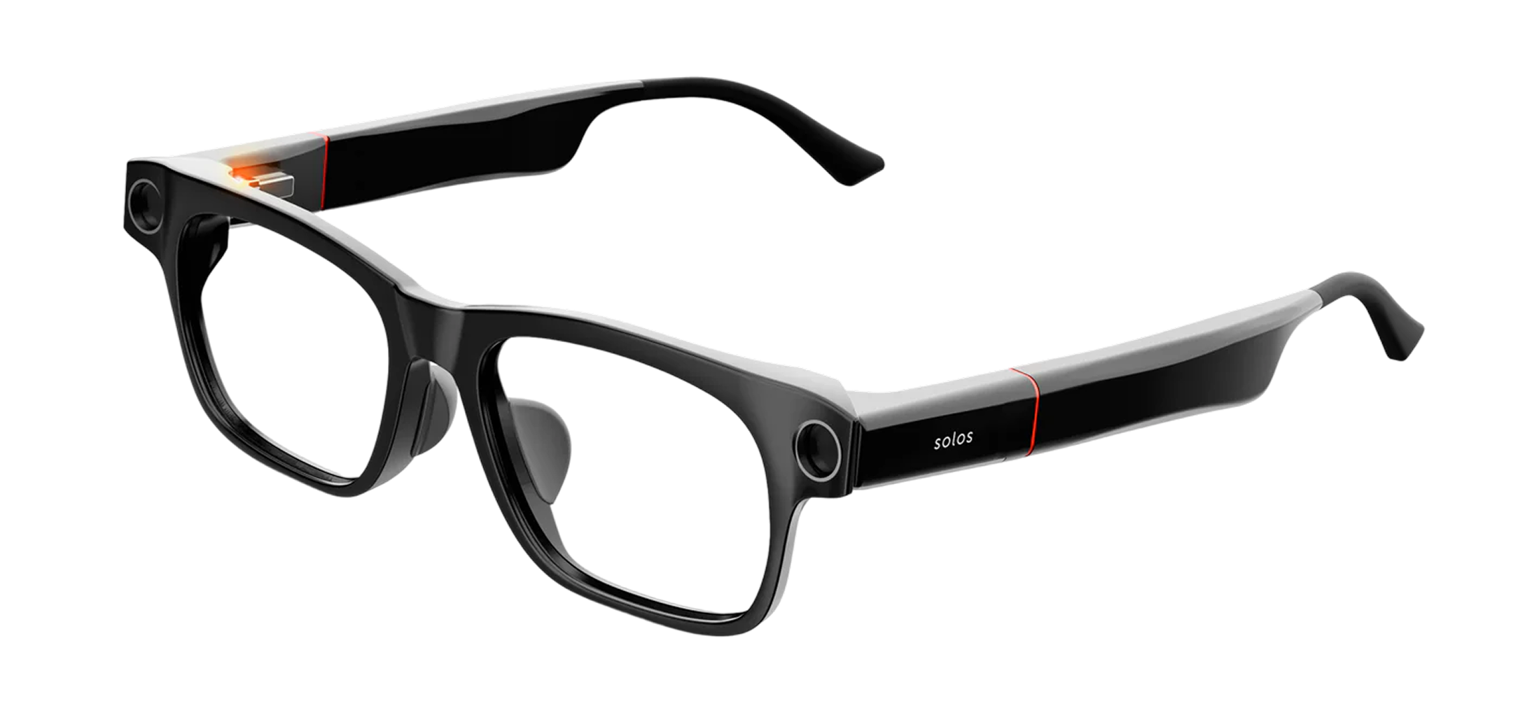 A pair of black Solos smartglasses with clear lenses, shown at an angle. The frames are sleek with built-in electronics housed in the temples, which feature a subtle red accent line and the "solos" logo. An orange indicator light is visible near the hinge on one side, suggesting the device is powered on or charging.
