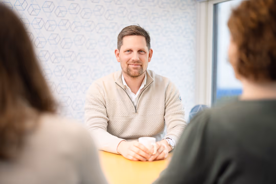 Kundemøte: rådgiver med kaffekopp lytter til to partnere – profesjonell bedriftsfoto Stavanger.