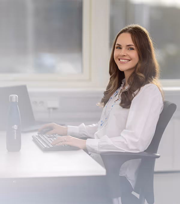 Kundekonsulent på lyst kontor smiler mot kamera mens hun jobber ved tastatur – bedriftsfoto og videoproduksjon Stavanger.