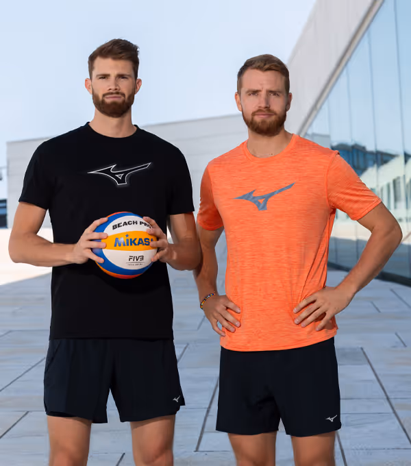 Portrett av to beachvolleyball-spillere i Mizuno-t-skjorter som holder Mikasa-ball foran moderne glassbygning – sportsfotografering og videoproduksjon Oslo.