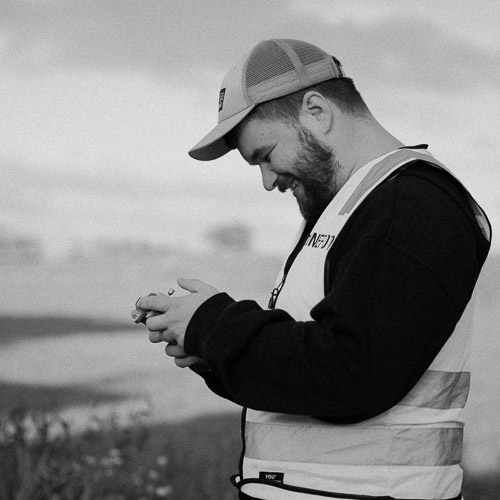 Bak kulissene-bilde av en fotograf fra Flare i Stavanger som kontrollerer utstyr under en utendørs fotoshoot. Fokus på autentiske øyeblikk og arbeid i felt.
