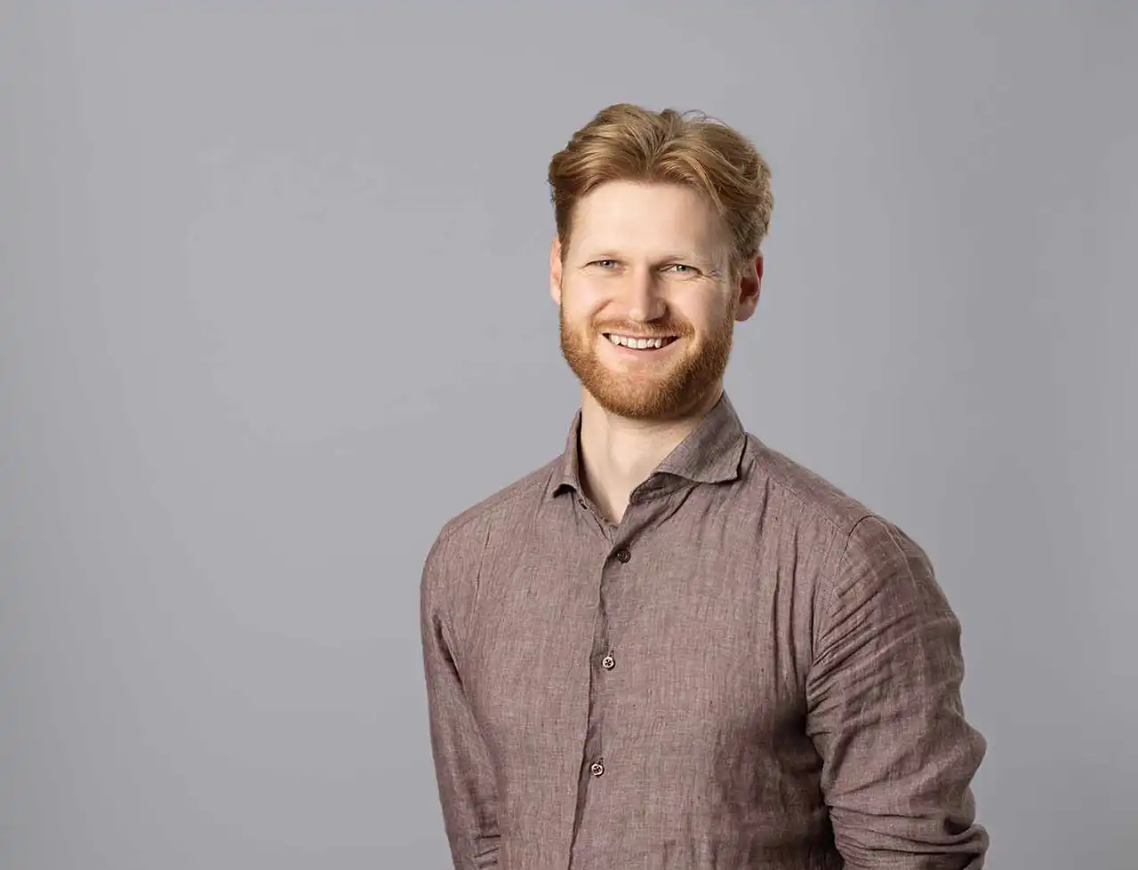 Profesjonelt ansattportrett Stavanger – ung mann med skjorte og skjegg smiler mot kamera.