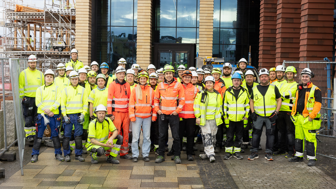 bedriftsfotograf fotograferer stort team i verneutstyr foran byggeplass for dokumentasjon av prosjekt og bedriftskultur