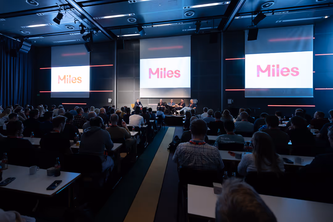Fullsatt sal under plenums­sesjon; tre storskjermer viser «Miles» – konferansevideo Stavanger.