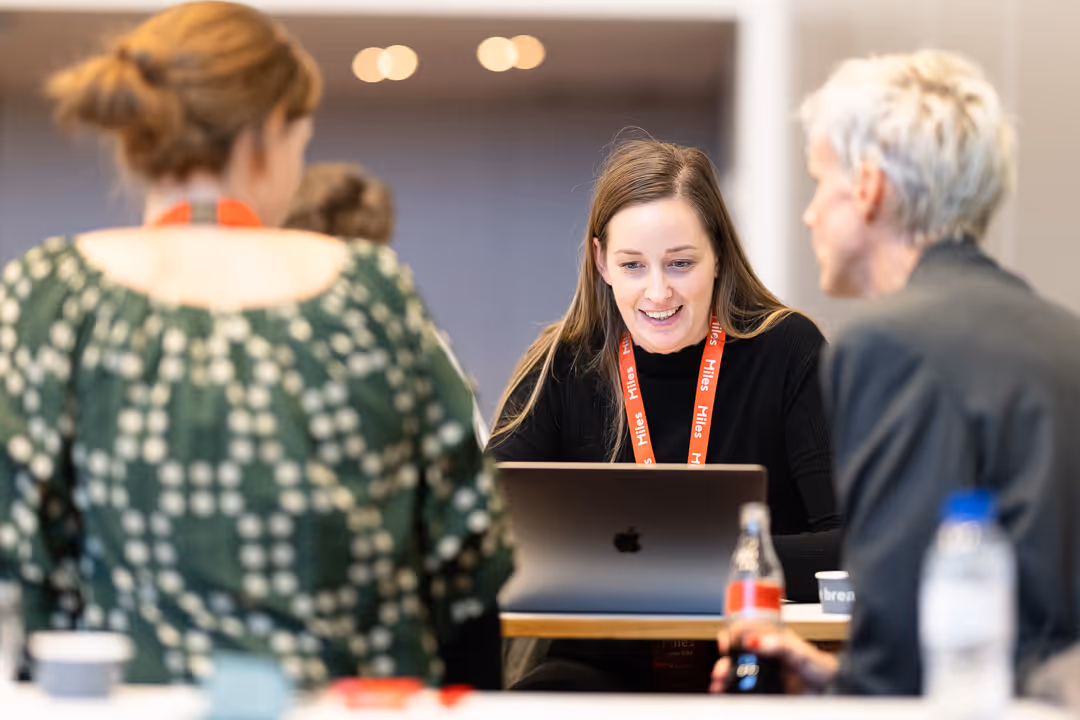 Deltakere med røde lanyards diskuterer prosjekt ved laptop under fagseminar – nettverksfoto.