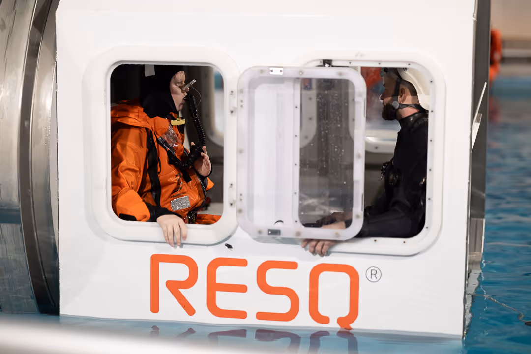 Kursdeltakere i oransje drakt inne i RESQ-evakueringskapsel før helikopter-sikkerhetstrening.
