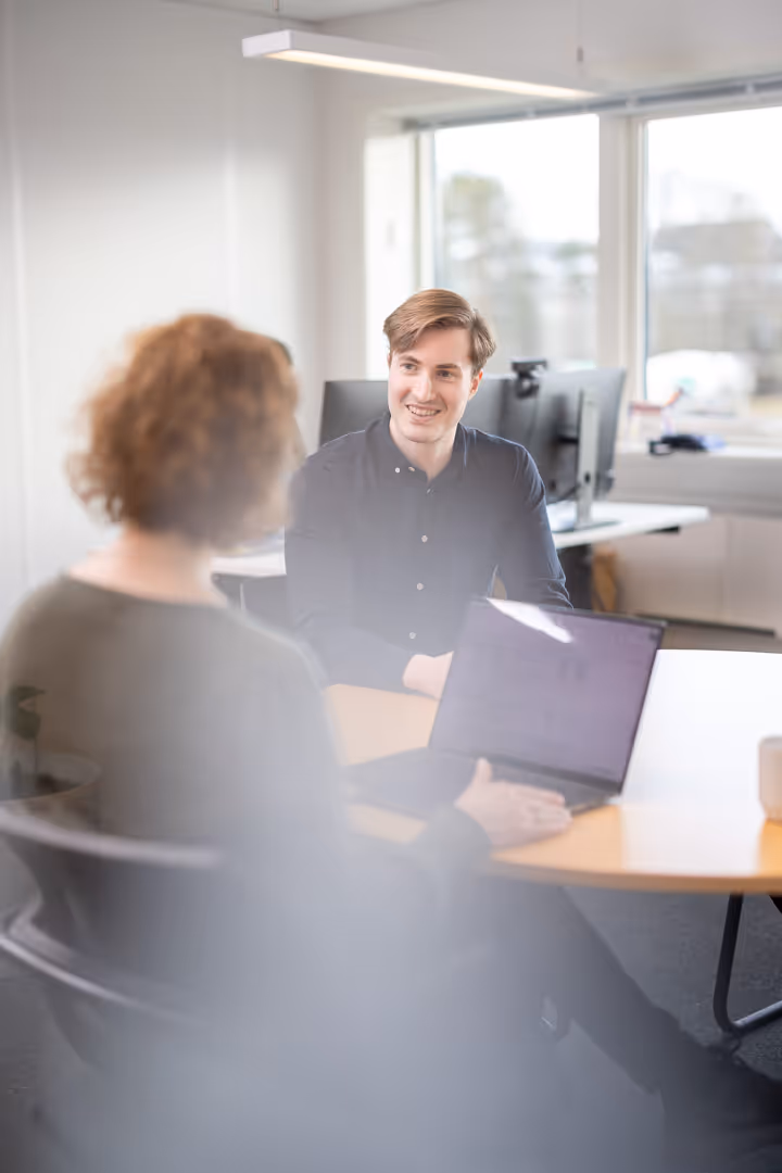 To konsulenter diskuterer prosjekt ved laptop i møterom – firmabilder Rogaland.