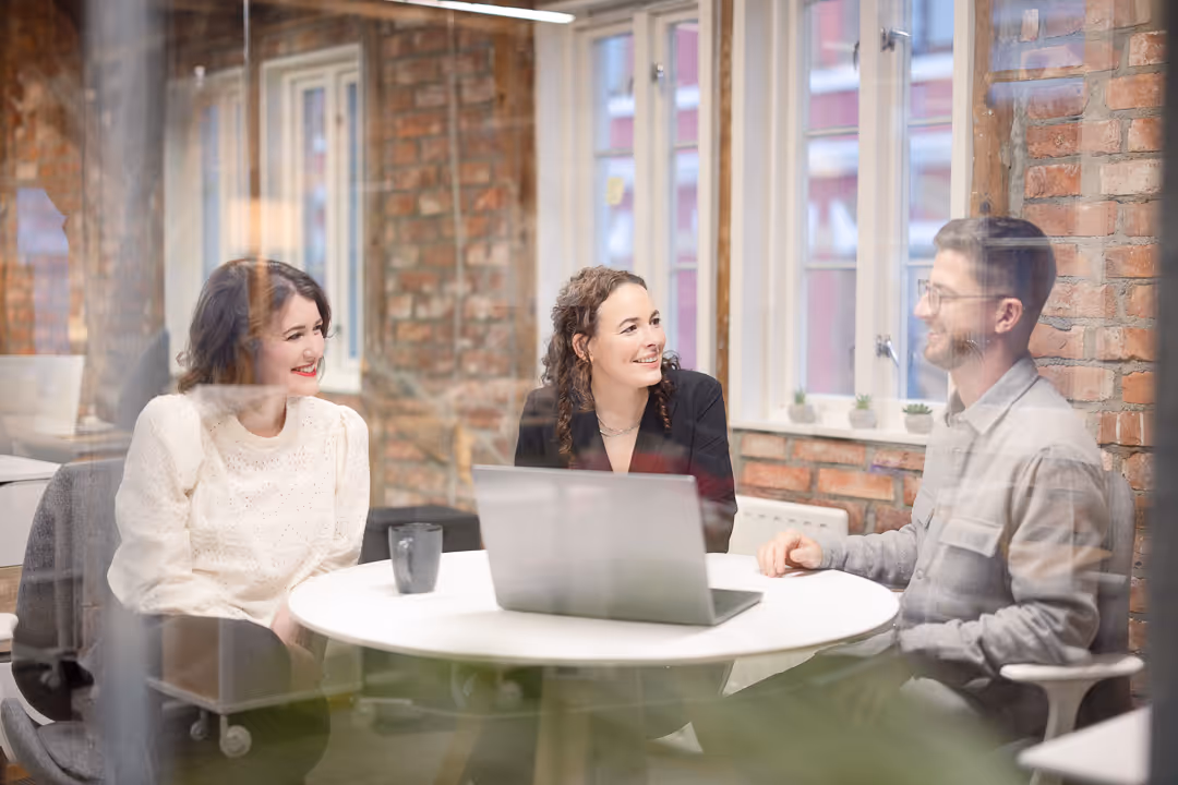 Teammøte rundt rund­bord med laptop i lyst lofts­kontor – bedriftsfoto Stavanger.