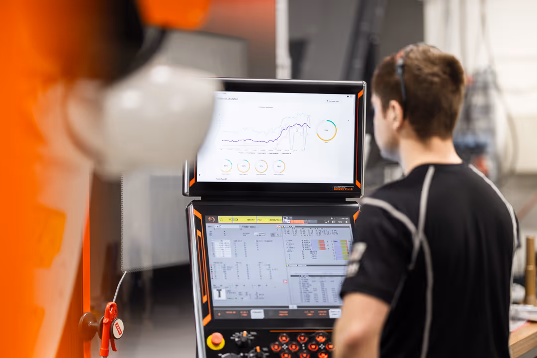 Operatør overvåker CNC-maskin via to skjermer med sanntids data – industriellfoto.
