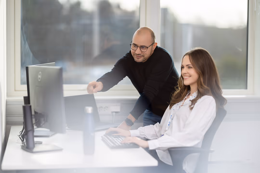 Mentor peker på skjerm mens trainee jobber ved PC – corporate fotografering Stavanger.