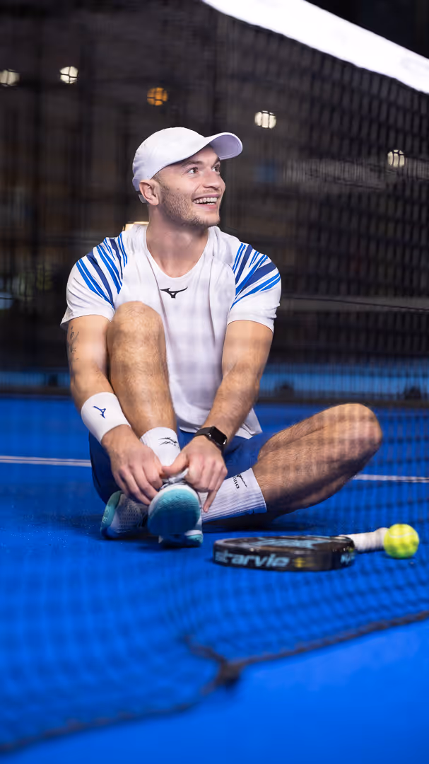 Padelspiller sitter på padel-bane og strammer sko ved racket – lifestyle-foto Rogaland.