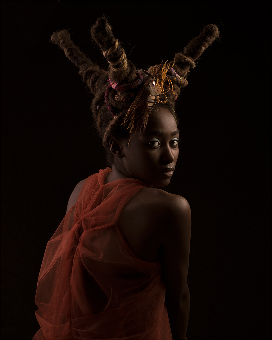 Dark editorial portrait of a model with a sculptural horned updo and bare shoulders