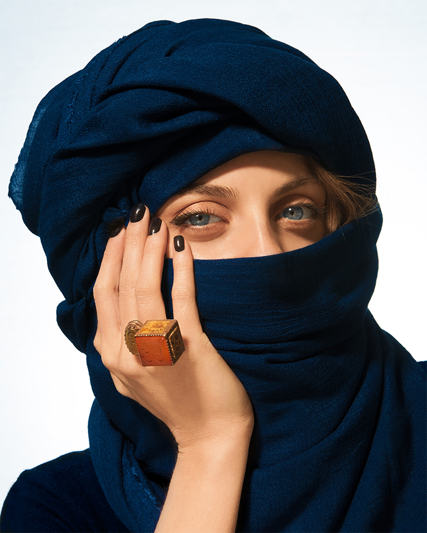 Editorial portrait of a model wrapped in a dark navy headscarf covering the lower face