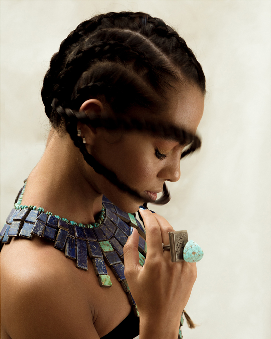 Profile portrait of a model with cornrow braids and metal jewelry on a light background