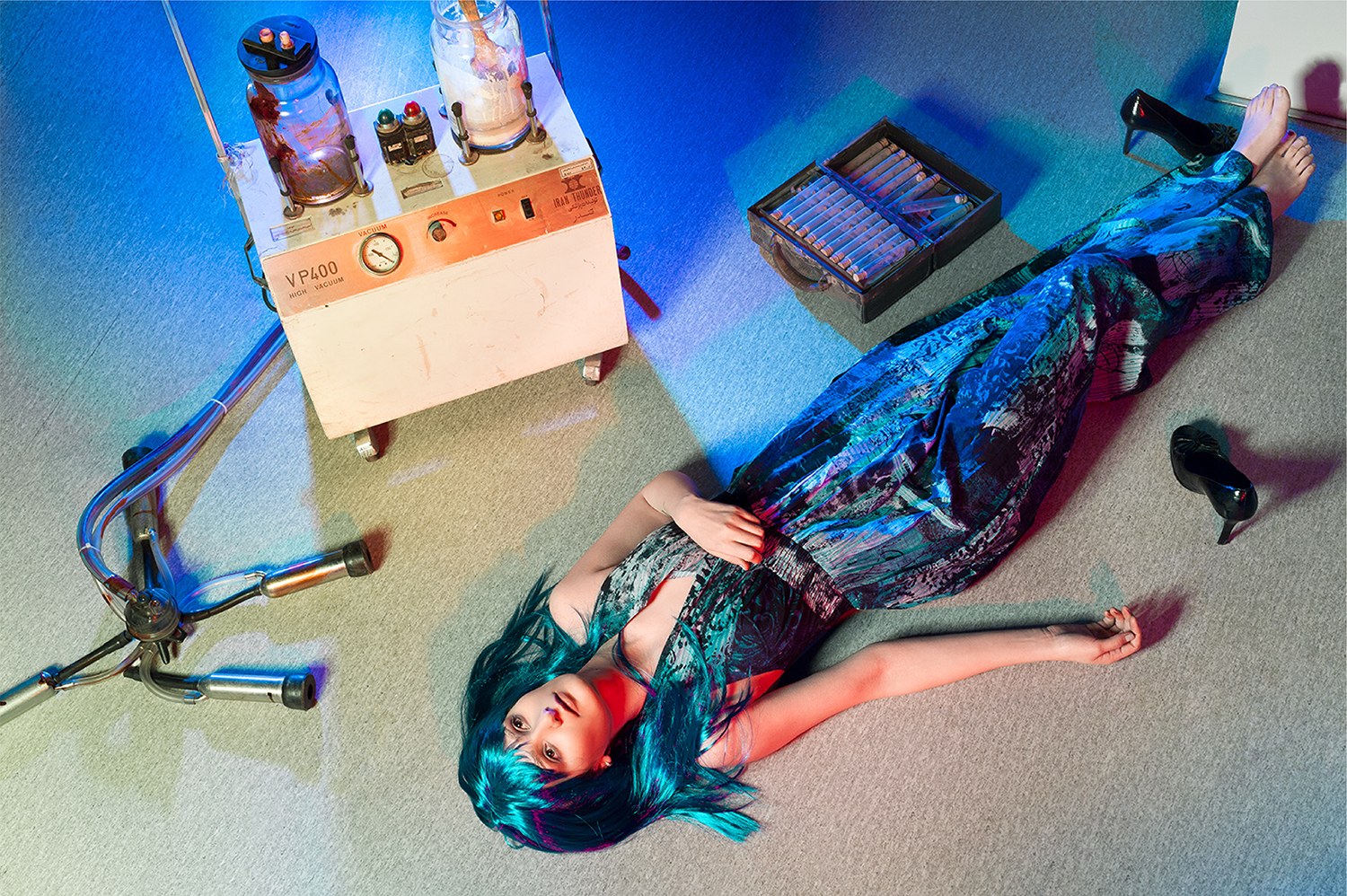 Surreal fashion editorial of a model with blue hair posed among colorful bottles and props